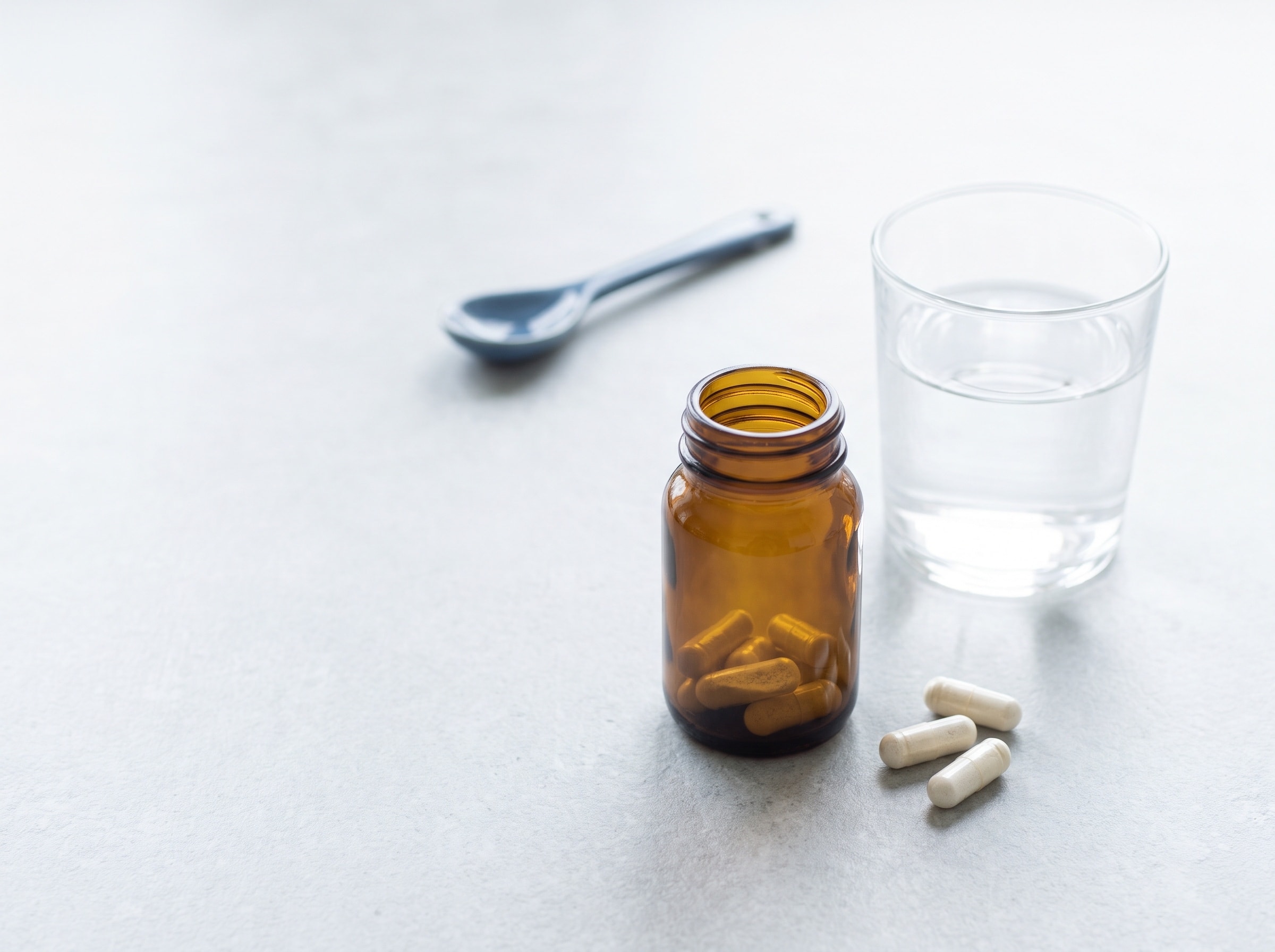 An amber supplement bottle with loose capsules beside a glass of water