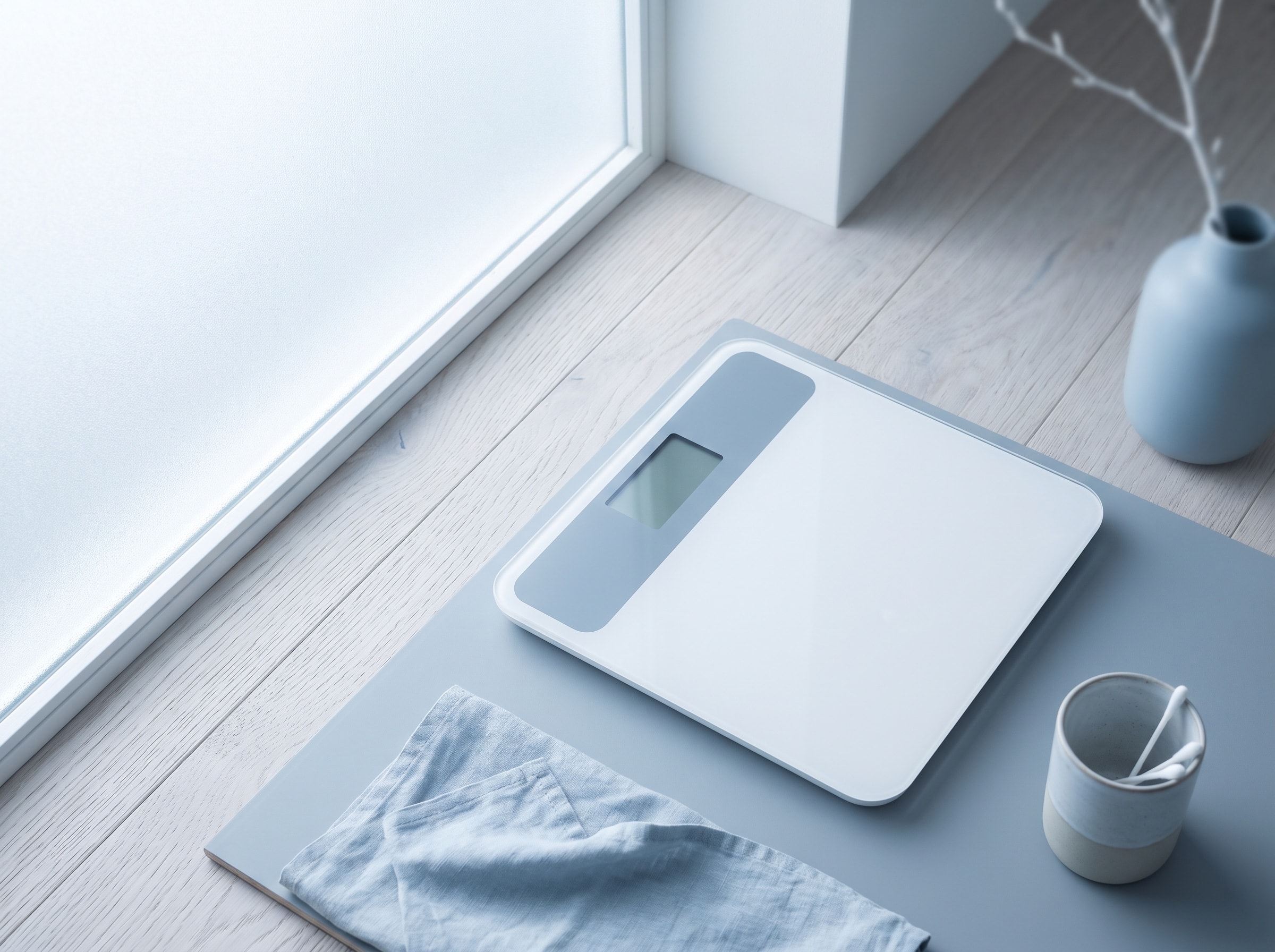 A digital scale on a pale wood floor beside a window, seen from above